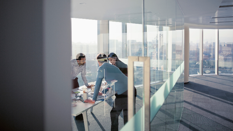 three business people standing over a table in a glass office